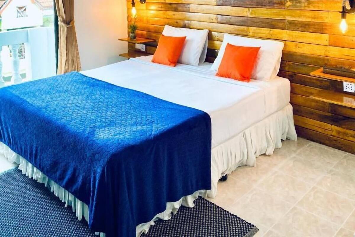 Un dormitorio con una cama, dos almohadas, una colcha azul, un cabecero de madera y dos cuadros en la pared.