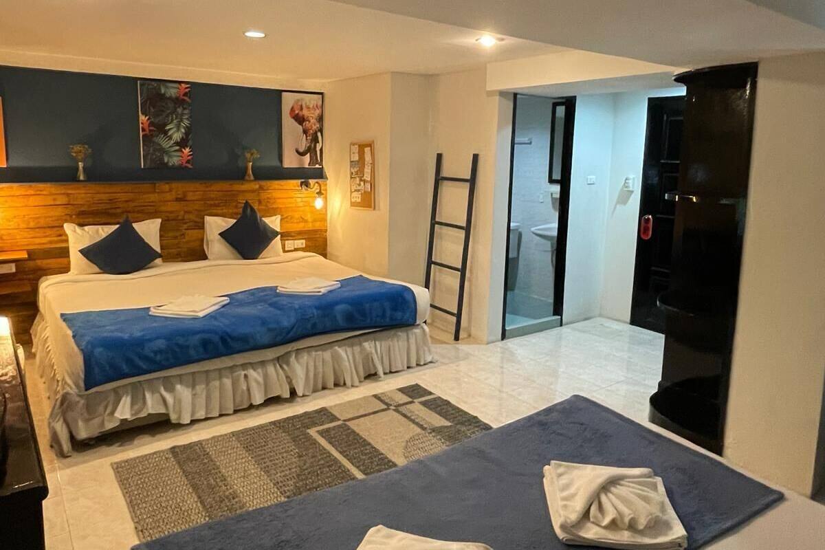 Habitación de hotel con dos camas, cabecero de madera, colcha azul, pared blanca con un cuadro y puerta que da a un balcón.
