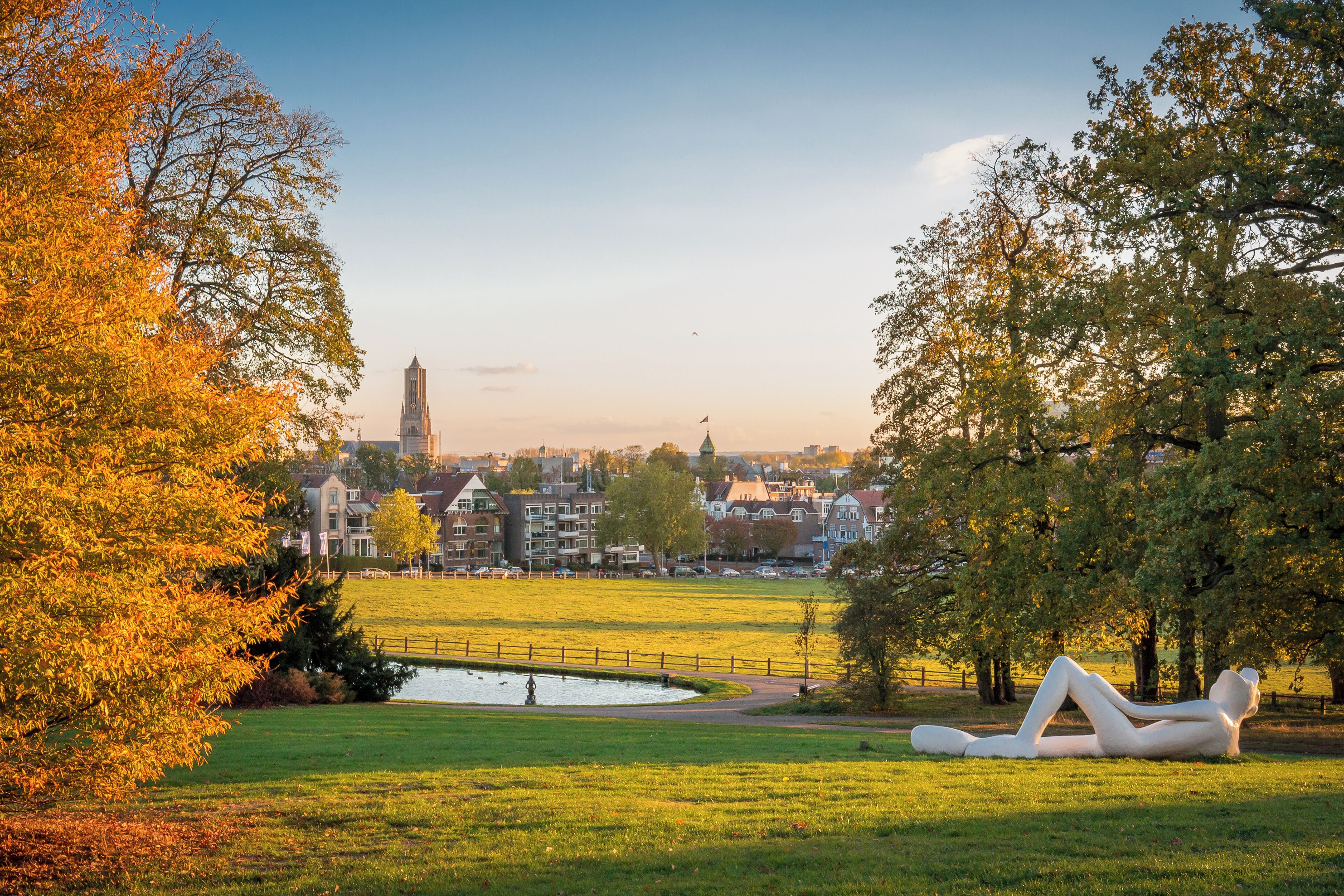 A park with a sculpture, a pond, and a distant building.