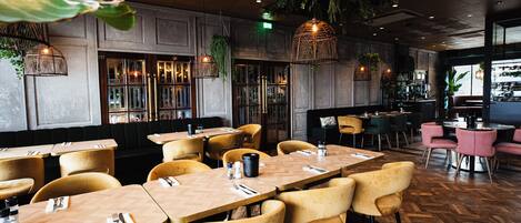 A restaurant interior with wooden tables and yellow chairs, a bar area, and hanging plants.