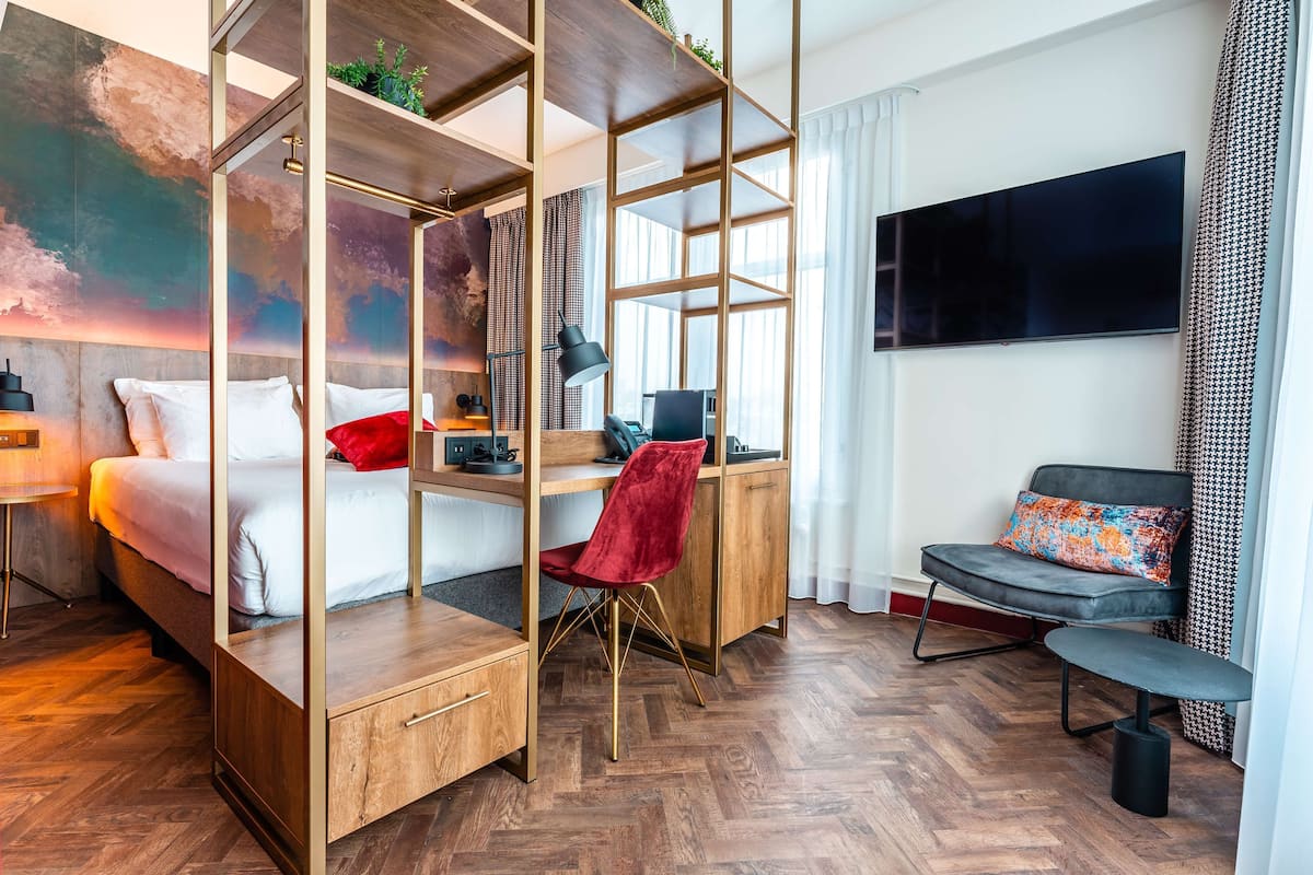 A modern hotel room with a bed, desk, chair, and TV.