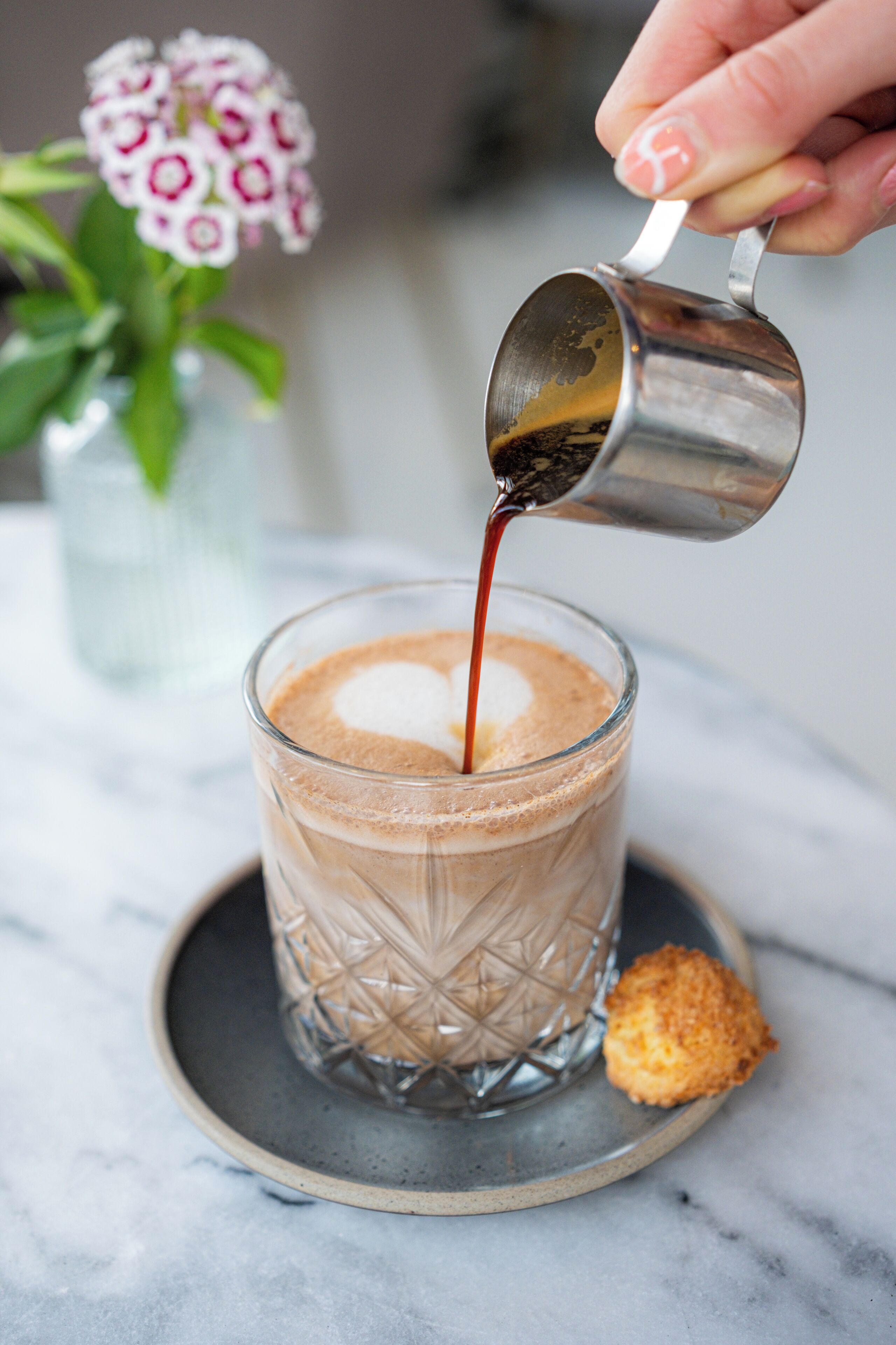 A clear glass mug with a textured pattern, filled with a beverage and a dollop of cream on top.