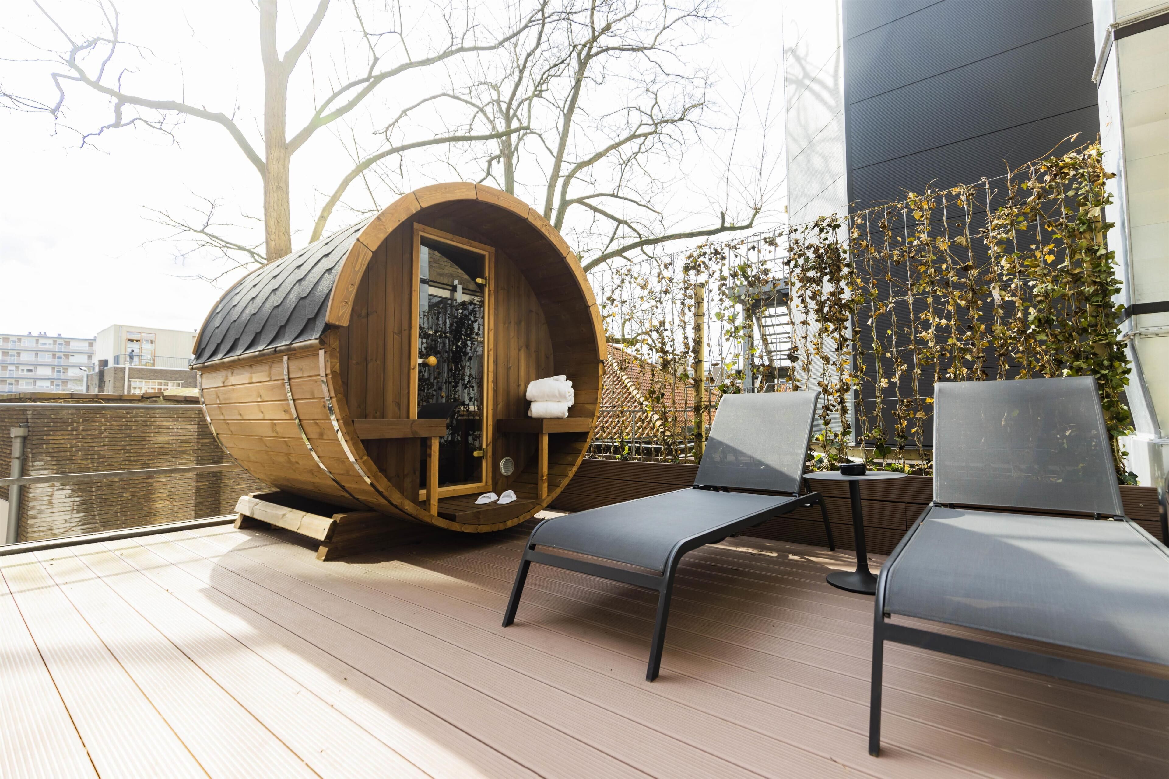 Un sauna en bois avec une porte en verre, deux chaises longues et une table sur une terrasse extérieure.