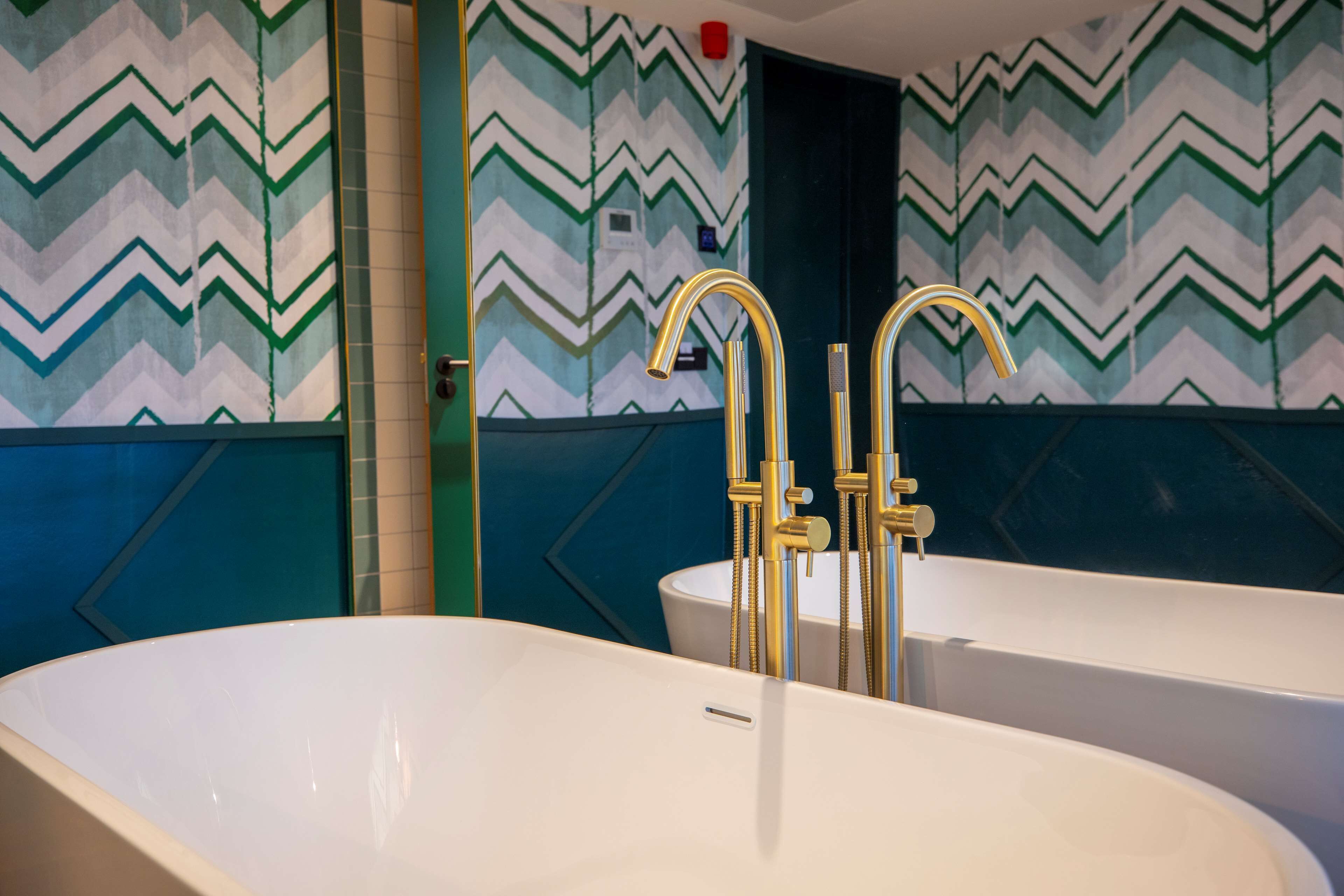 A bathroom with two white sinks and a bathtub, featuring a chevron-patterned wall and gold fixtures.