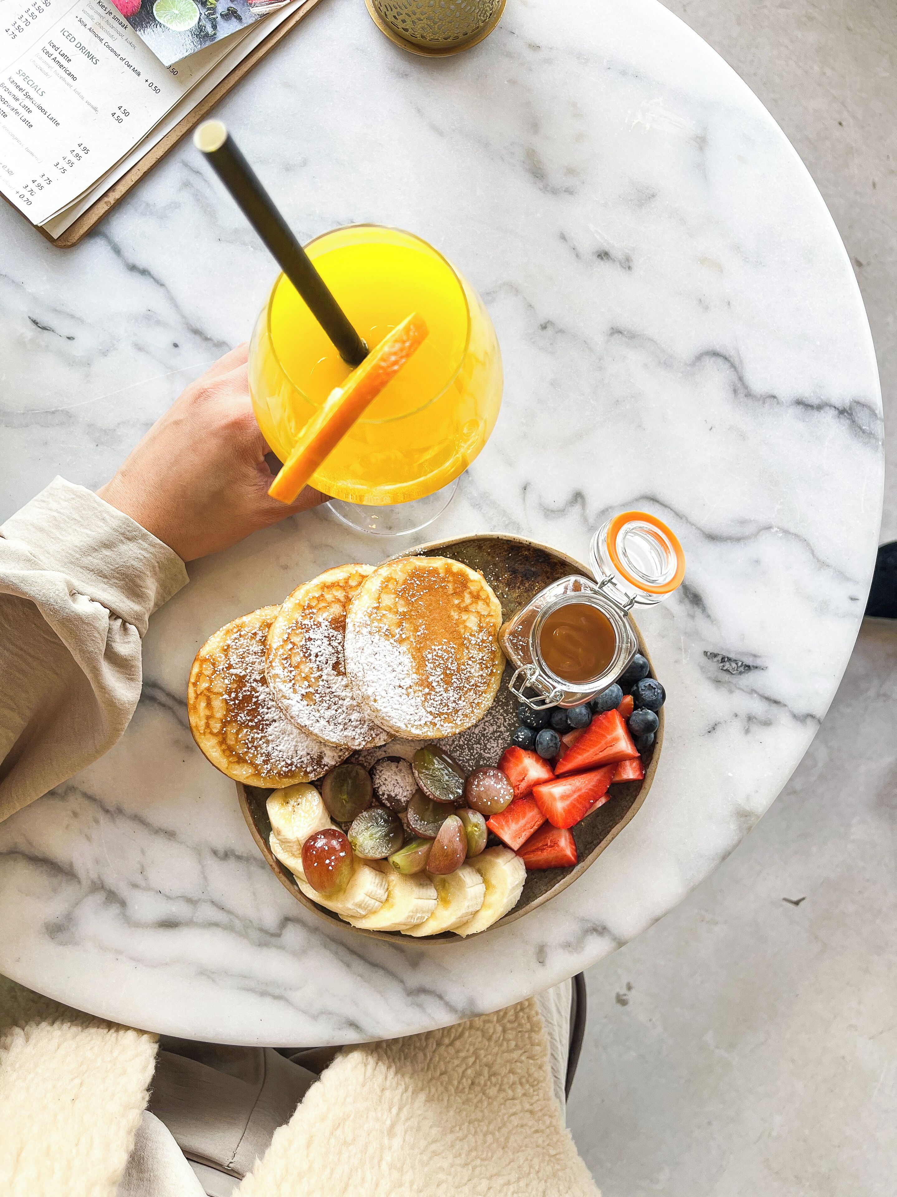 A breakfast setting with pancakes, fruit, and a drink on a marble table.