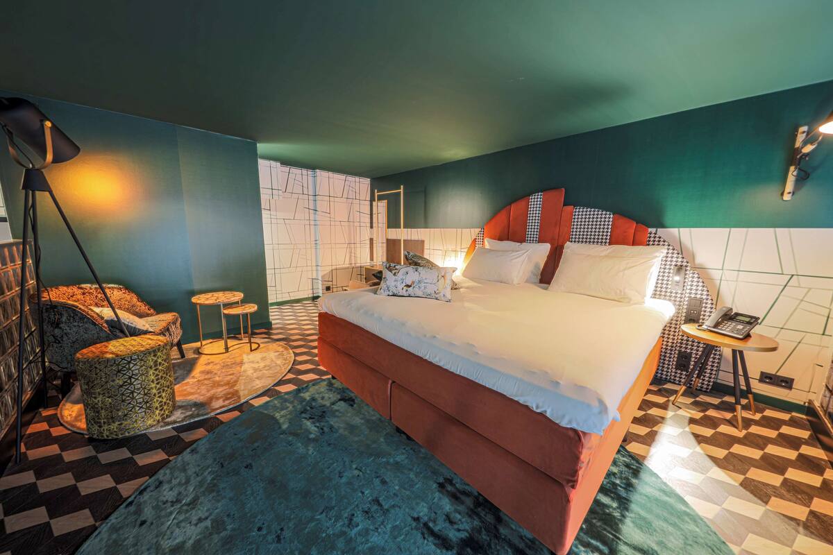 A modern hotel room with a large bed, a desk, and a patterned rug.