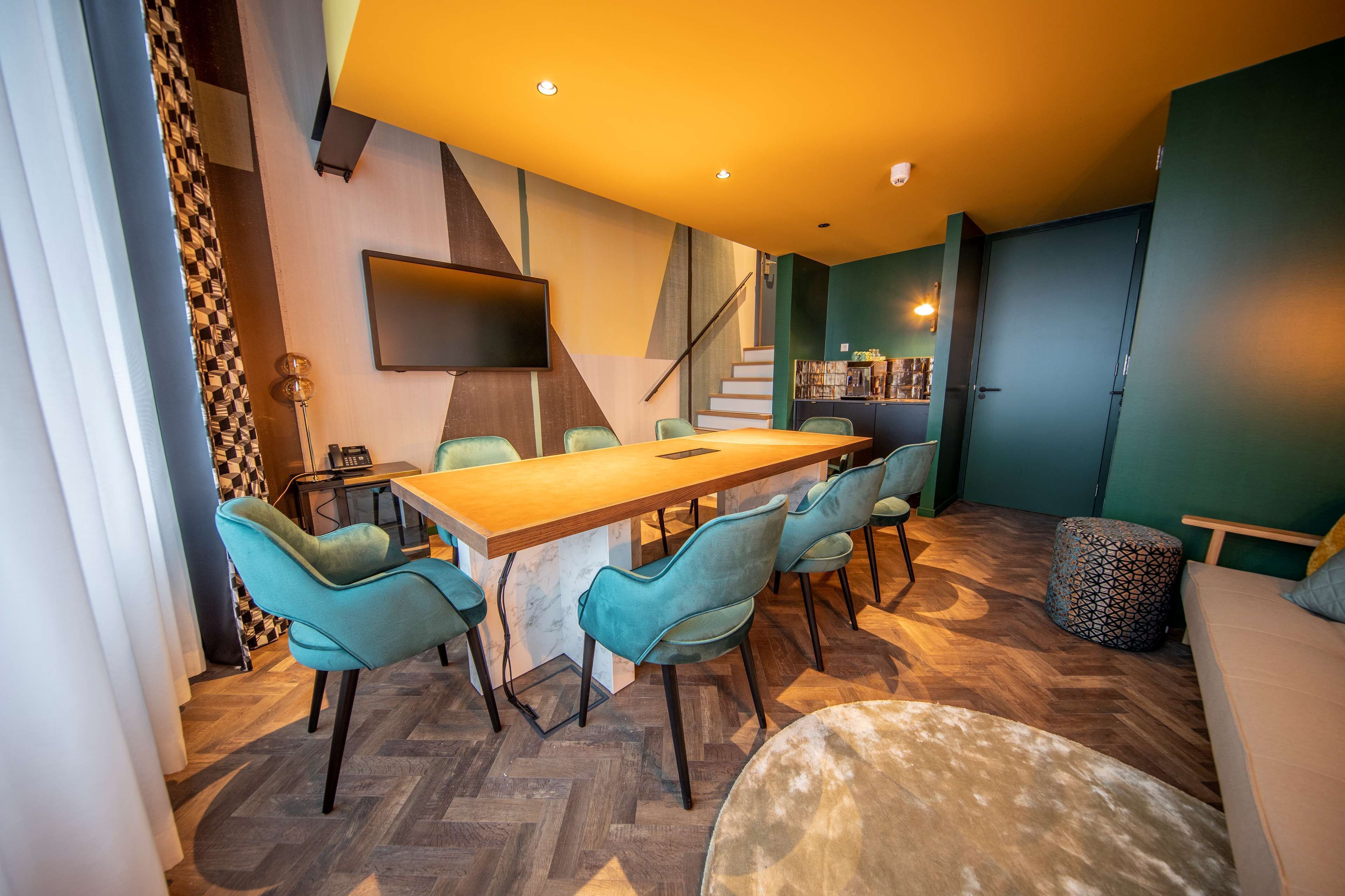 Un comedor moderno con una mesa de madera y sillas color turquesa, una escalera y una estantería.