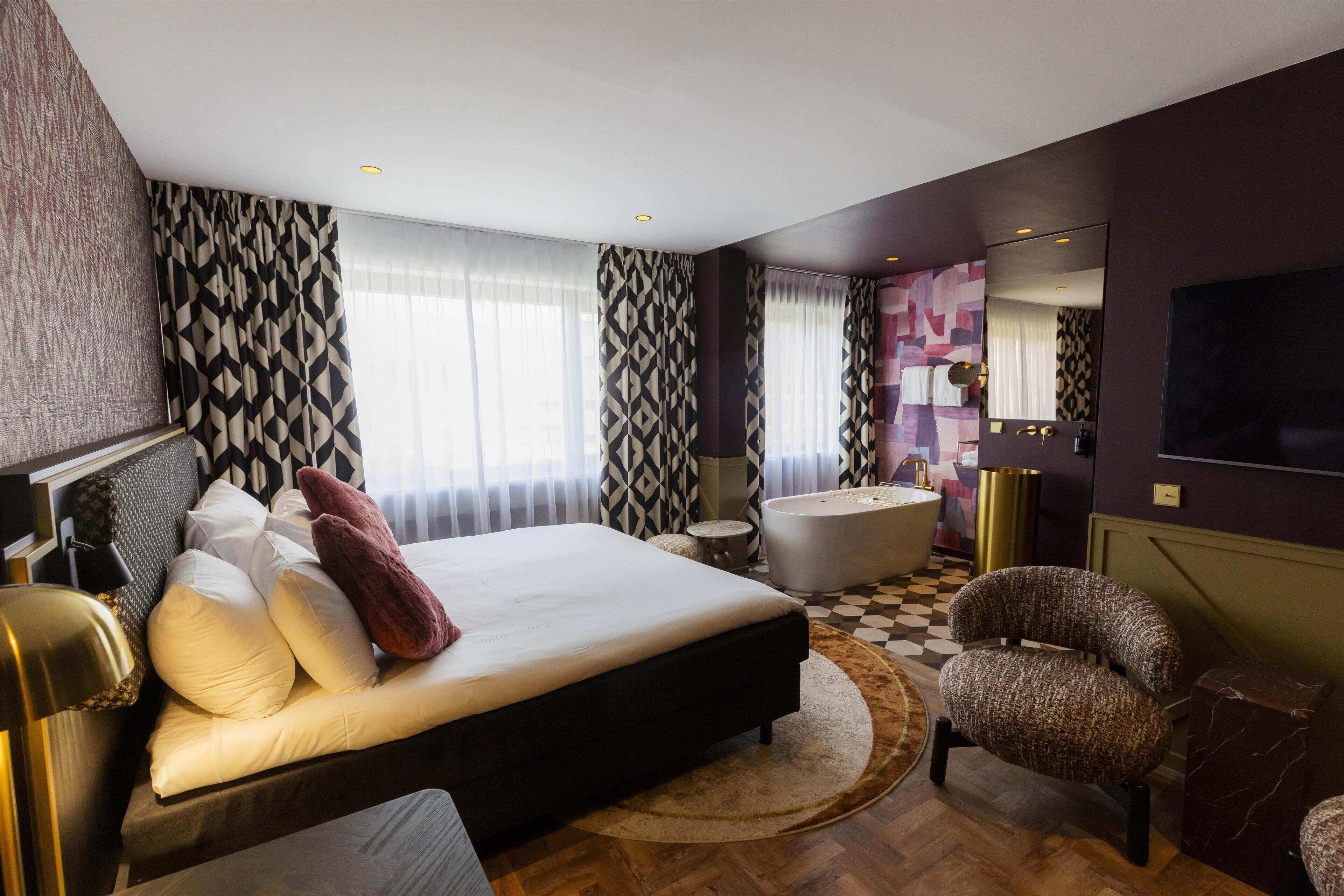 A modern hotel room with a large bed, a sitting area, a round rug, and a television.