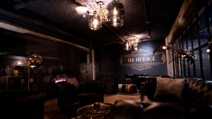 Un área de salón tenuemente iluminada con decoración vintage, que presenta un letrero grande que dice "The Storage" y una zona de bar con taburetes y una barra.