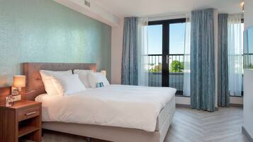 Una habitación de hotel moderna con una cama grande, una mesita de noche y una ventana con cortinas.