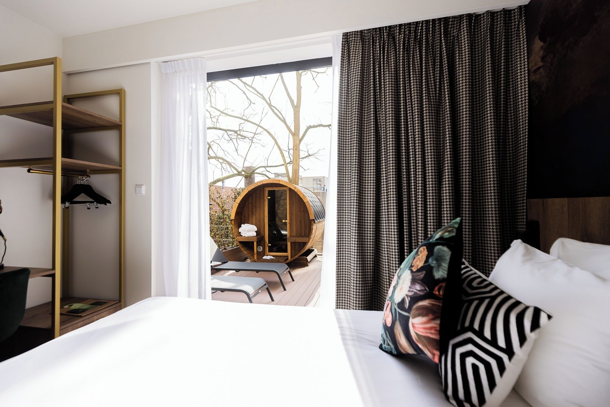 A hotel room with a bed, a wooden wardrobe, a seating area with a table and chairs, and a view of the outdoors.