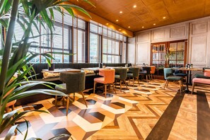 A modern interior with a geometric patterned floor, a seating area with various chairs, and large windows providing natural light. - City Hotel Haarhuis - World Hotels Crafted Collections (Arnhem)