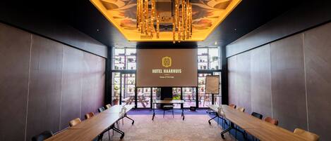 A conference room with a long table, chairs, and a projector screen displaying "HOTEL HAARHUIS House of Heritage".
