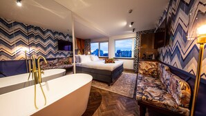 Un baño moderno con una bañera independiente, un sofá y una cama con vistas a la ciudad.