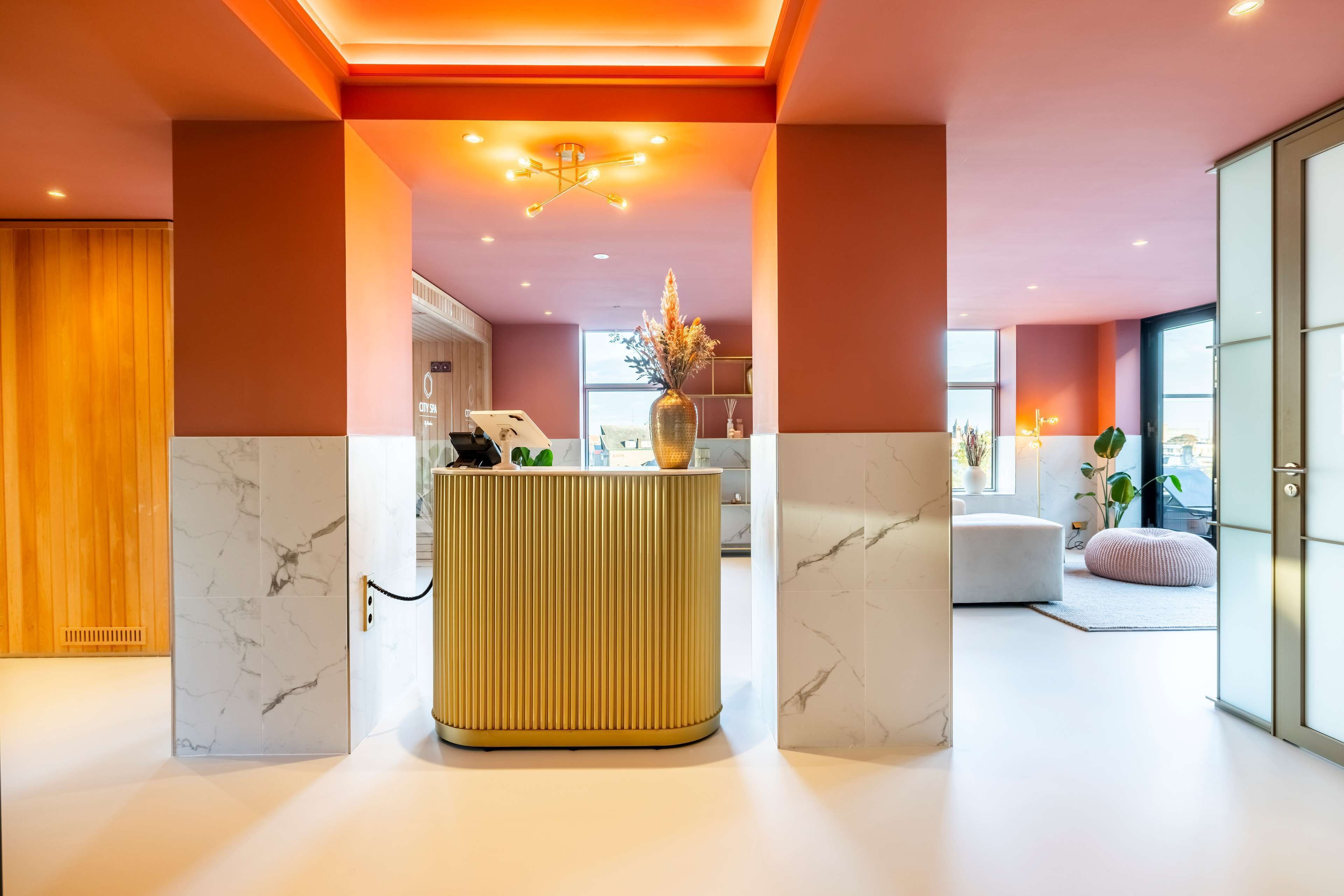 A modern reception area with a central counter, a wooden panel wall, and a view of the adjacent room.