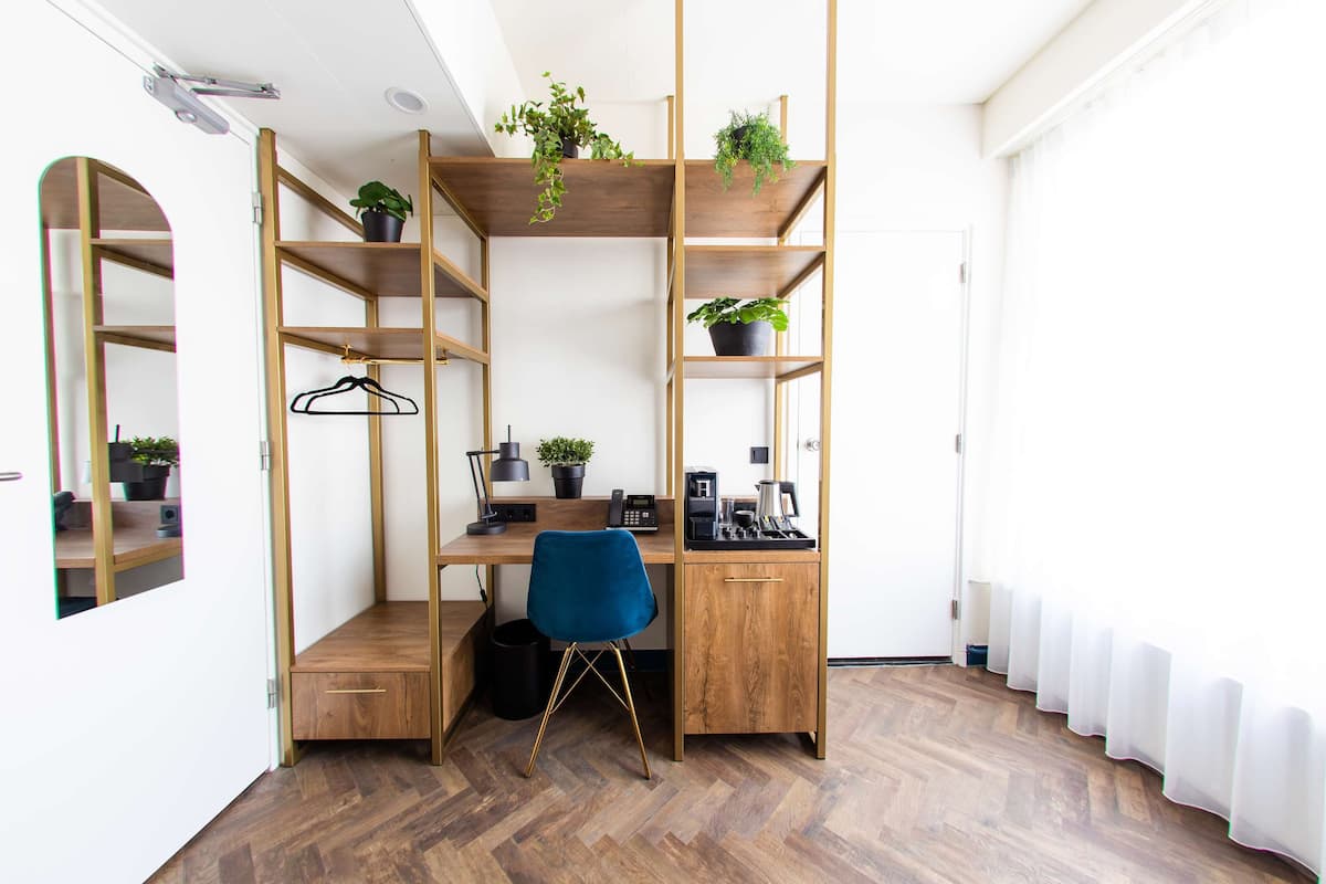 A compact, well-organized workspace with a desk, chair, and shelving unit, featuring plants and a mirror.