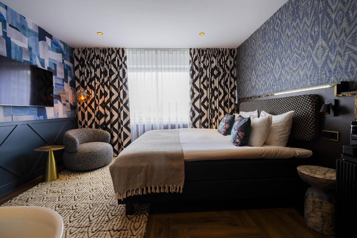 A modern bedroom with a large bed, a TV mounted on the wall, and patterned curtains.