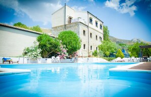 A swimming pool with a stone building in the background, surrounded by greenery and a clear sky. - Agriturismo Sant'Agata (Piana degli Albanesi)