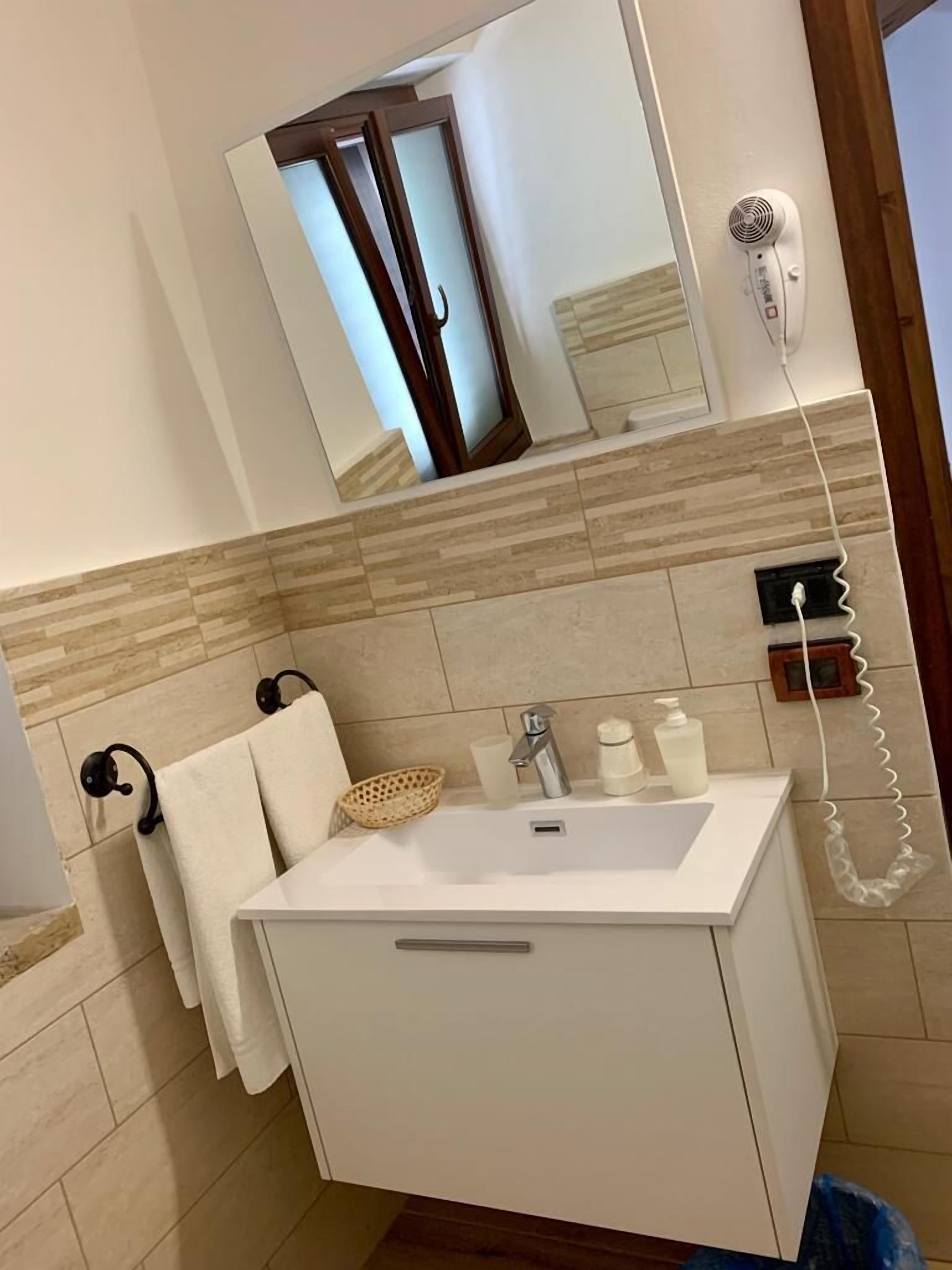 Un baño con lavamanos blanco, espejo, secador de pelo y toallero.