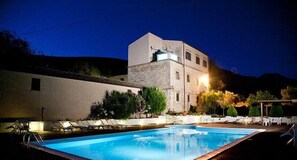 Un espace piscine avec des chaises longues et un bâtiment doté d’une façade en pierre.