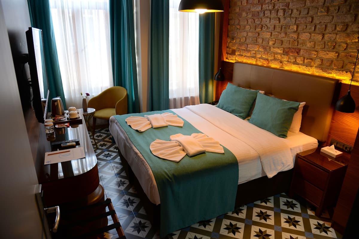 Une chambre d’hôtel avec un lit, un bureau et une chaise, une télévision et un mur en briques.