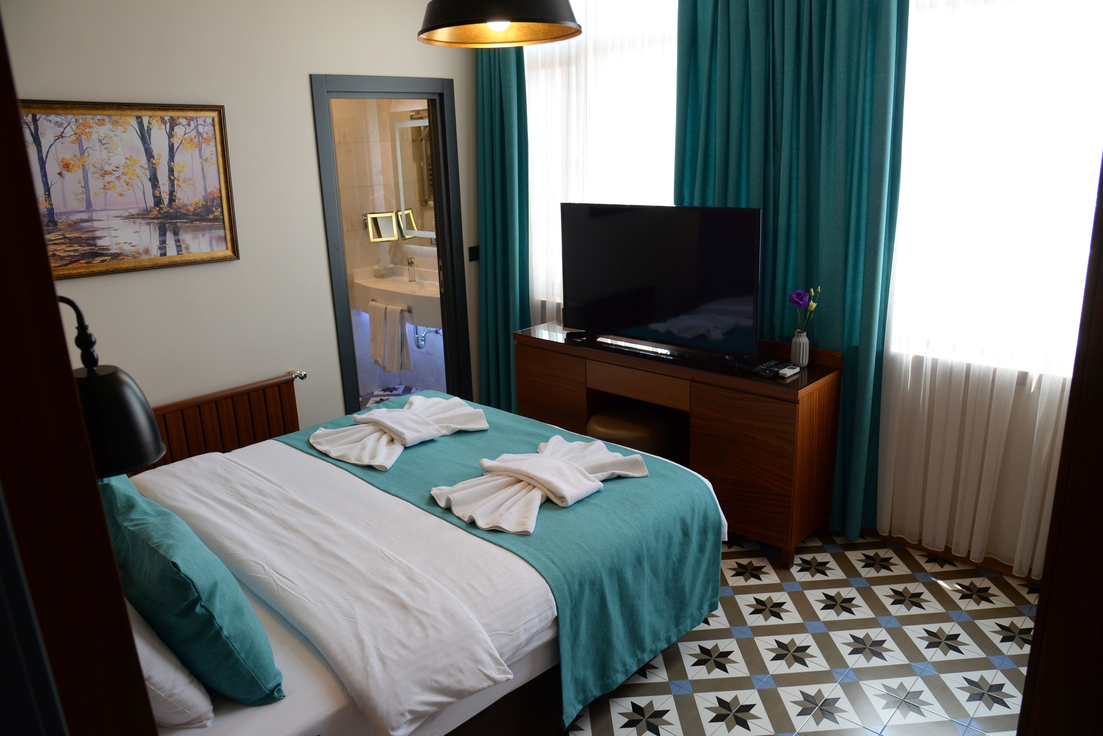 A hotel room with a bed, a television, a desk, and a bathroom visible through an open door.