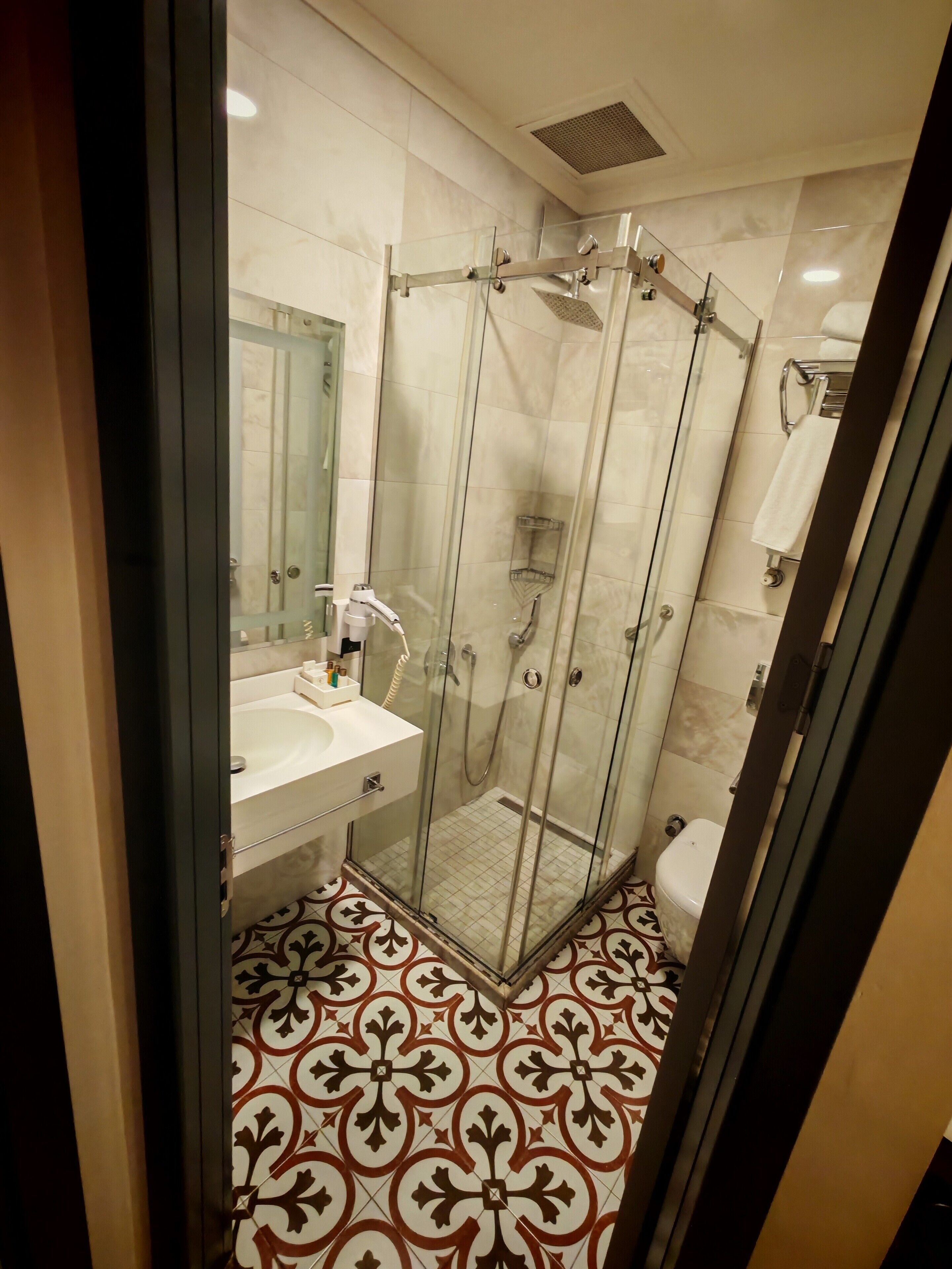 A modern bathroom with a glass-enclosed shower, a white sink, and a patterned floor.