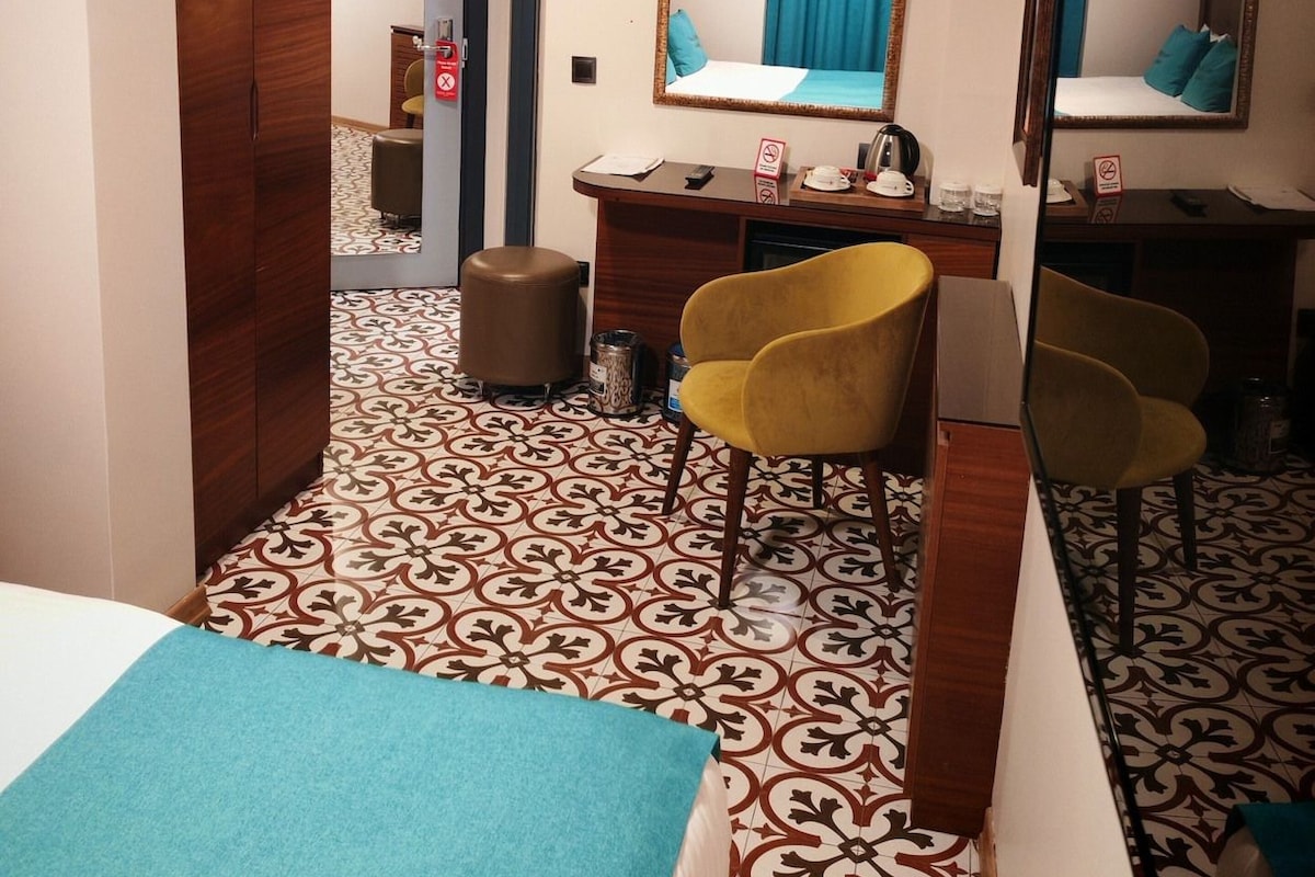 A hotel room with a bed, a desk, a chair, a mirror, and a patterned floor.