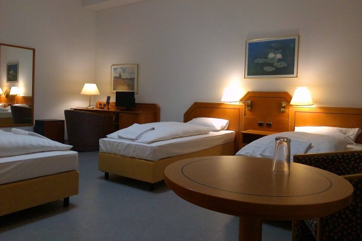 Een hotelkamer met twee eenpersoonsbedden, een klein rond tafeltje, een bureau met een stoel, en een televisie.