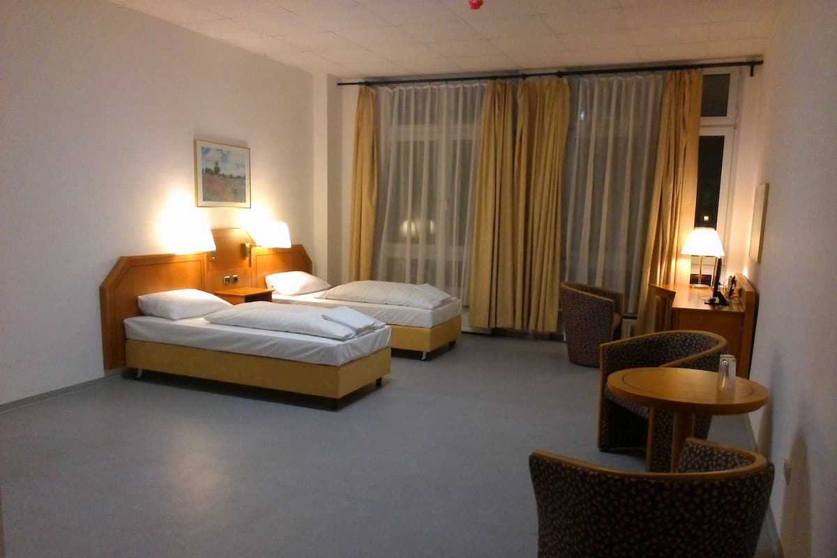 Een hotelkamer met twee bedden, een stoel, een tafeltje en een lamp.