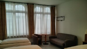 Une chambre d’hôtel avec deux lits simples, un canapé, une petite table ronde et un téléviseur fixé au mur.