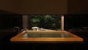 A modern bathroom with a large rectangular bathtub, a small stone structure, and lush green plants in the background. - The Edo Sakura (Tokyo)