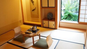 A traditional Japanese room with tatami flooring, a low table with a kettle, a decorative fish on the wall, and a view of greenery outside. - The Edo Sakura (Tokyo)