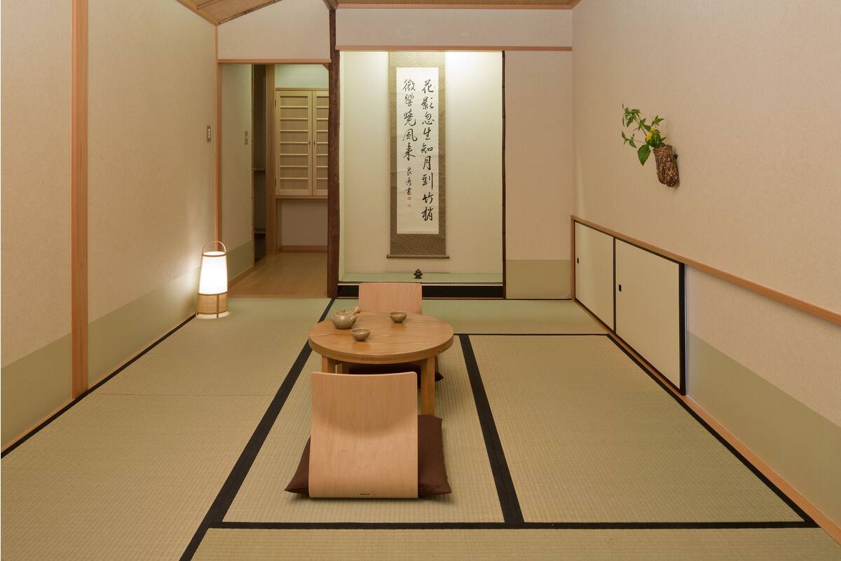 Una habitación japonesa tradicional con suelo de tatami, una mesa baja con un juego de té y una puerta corredera que da a otra habitación.
