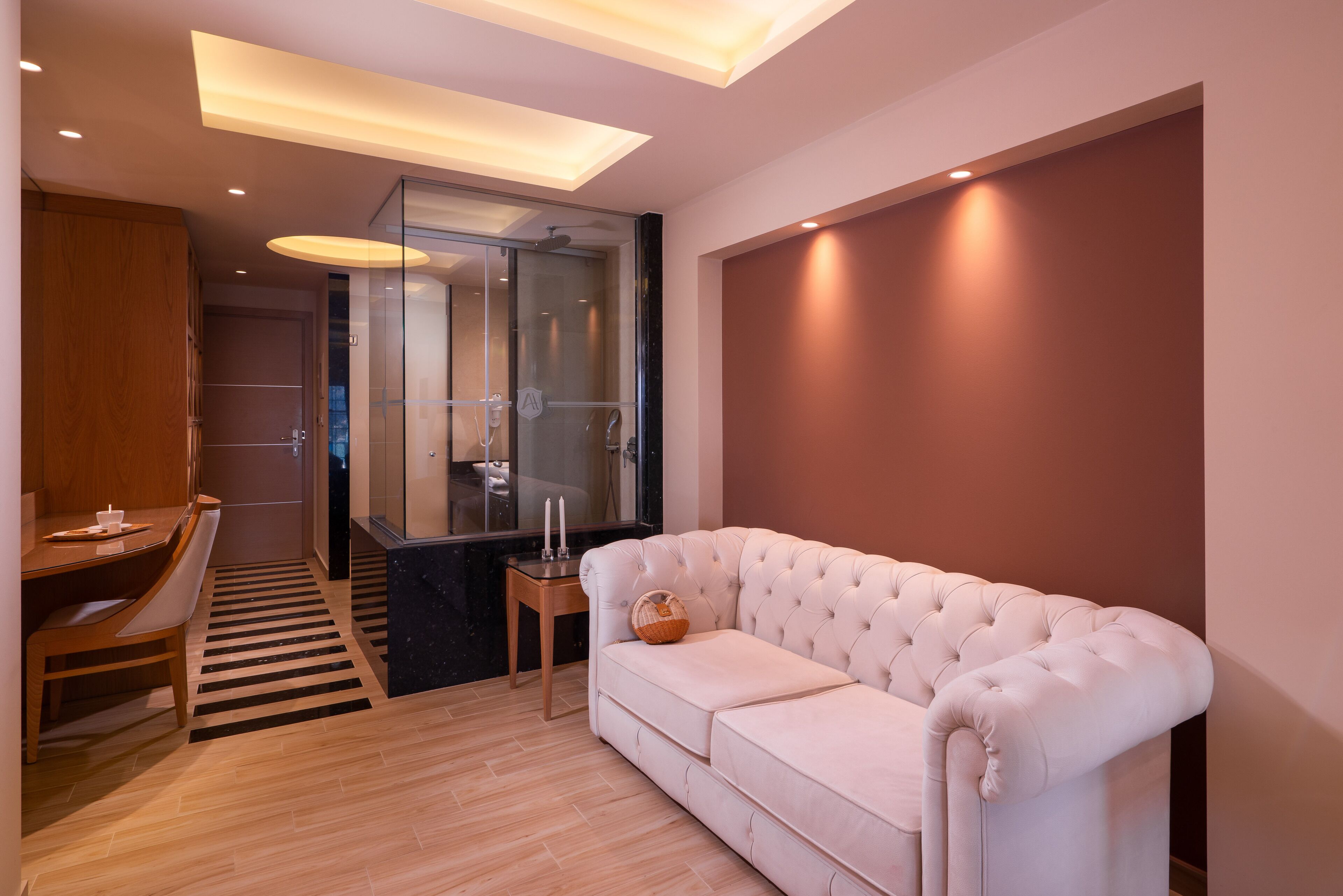 Una habitación moderna con un sofá blanco, un escritorio de madera y una cabina de ducha de vidrio.