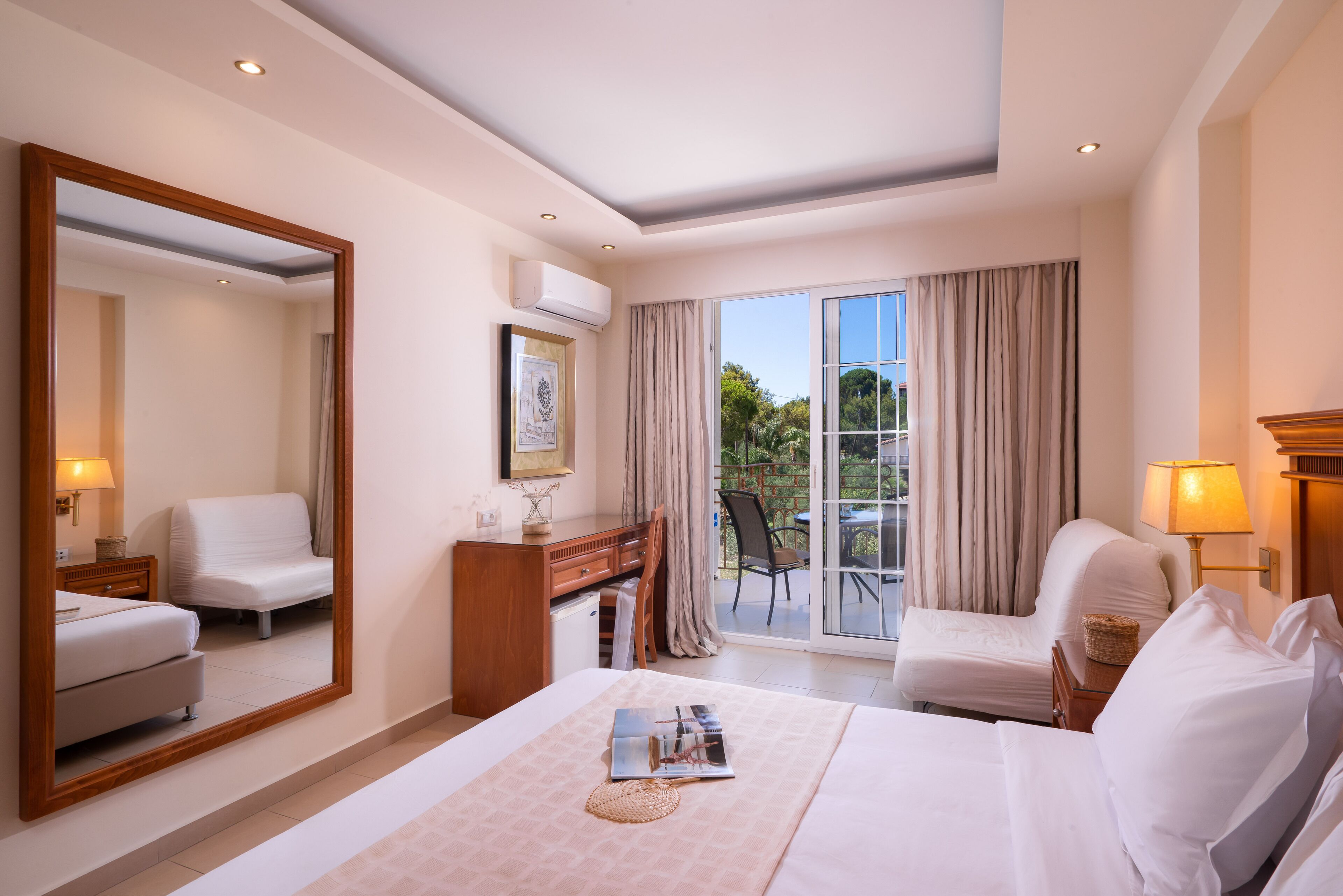 A hotel room with a large bed, a desk, a chair, a mirror, and a balcony with curtains.