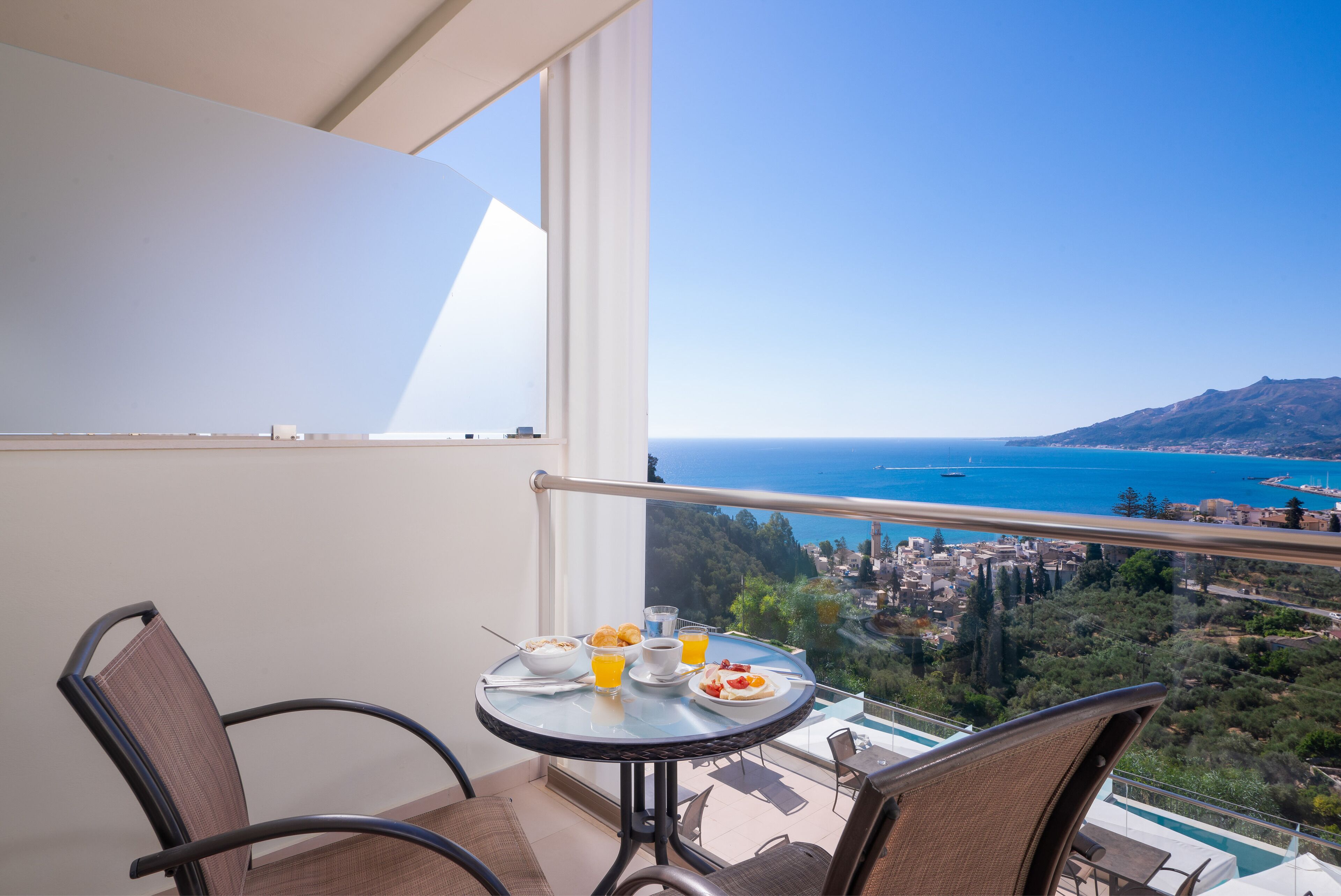 Un balcón con una mesa lista para el desayuno, con vista a un pueblo costero y al mar.