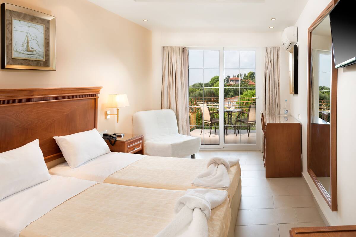 A hotel room with two beds, a sitting area, a TV, and a balcony with a view.