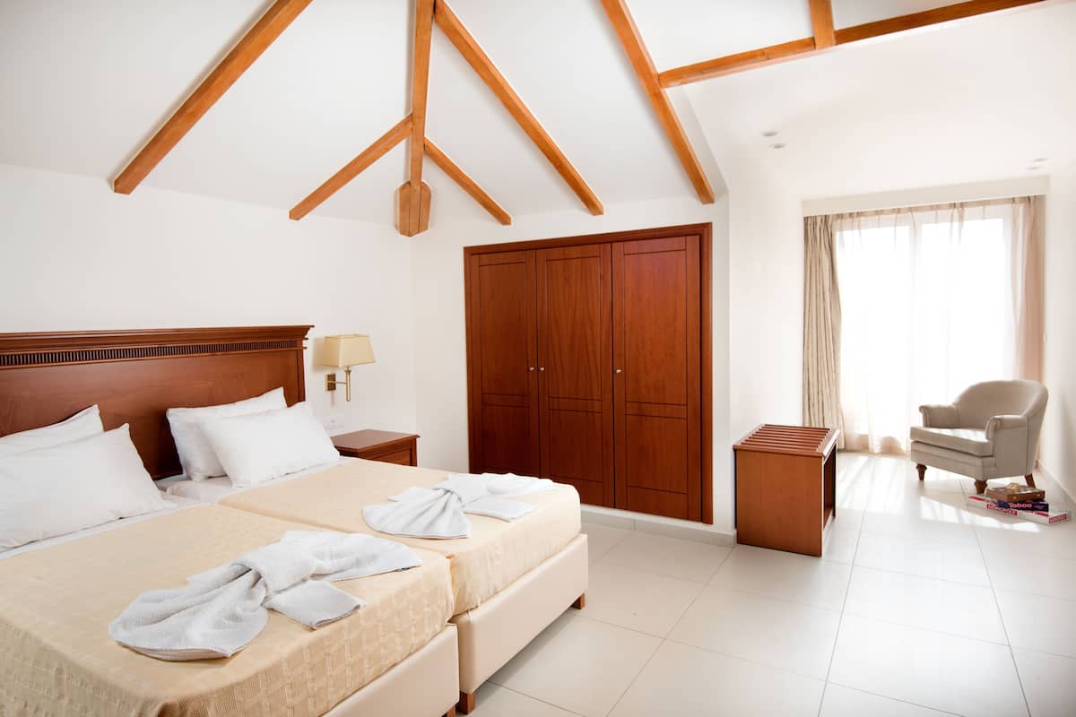 A hotel room with a large bed, wooden wardrobe, a sitting area with a chair, and a small wooden side table.