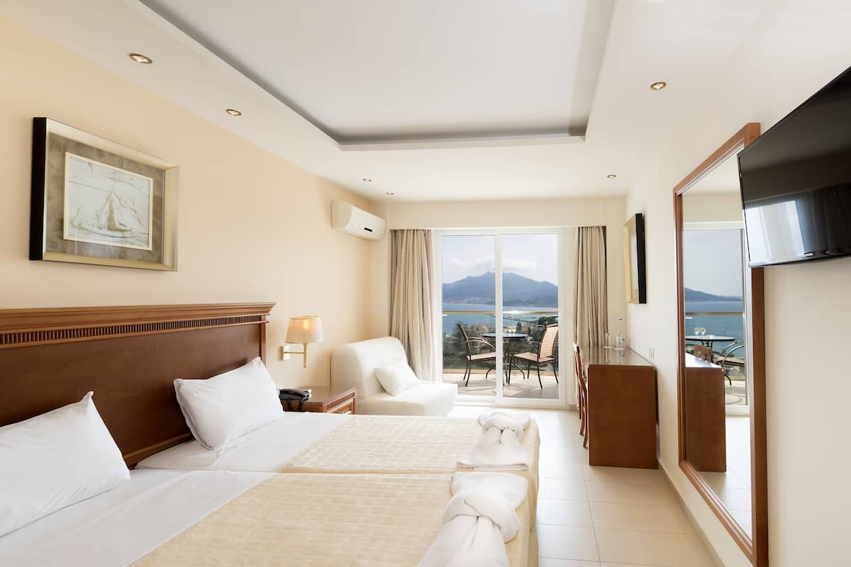 A hotel room with a large bed, a TV, a balcony with a view of the sea, and a painting on the wall.