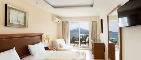 A hotel room with a large bed, a TV, a balcony with a view of the sea, and a painting on the wall.