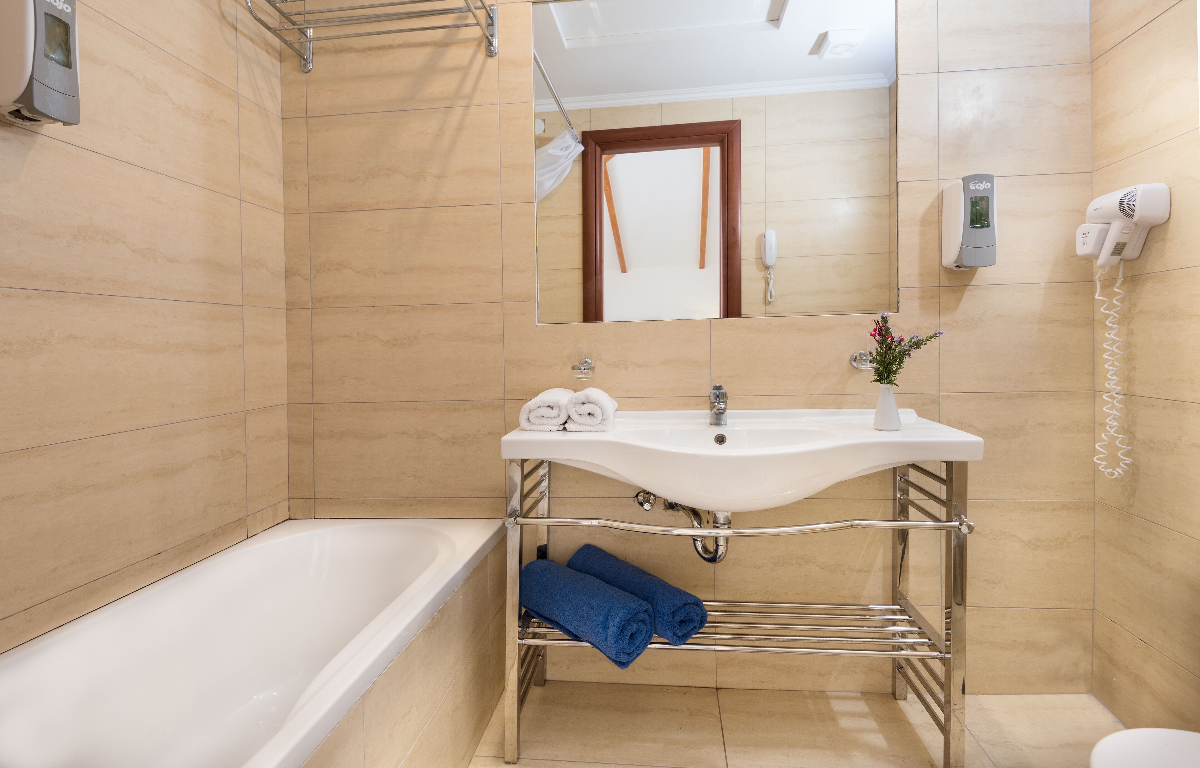 Ein Badezimmer mit einer Badewanne, einem Waschbecken mit Spiegel darüber, einem Handtuchhalter und einem an der Wand befestigten Föhn.