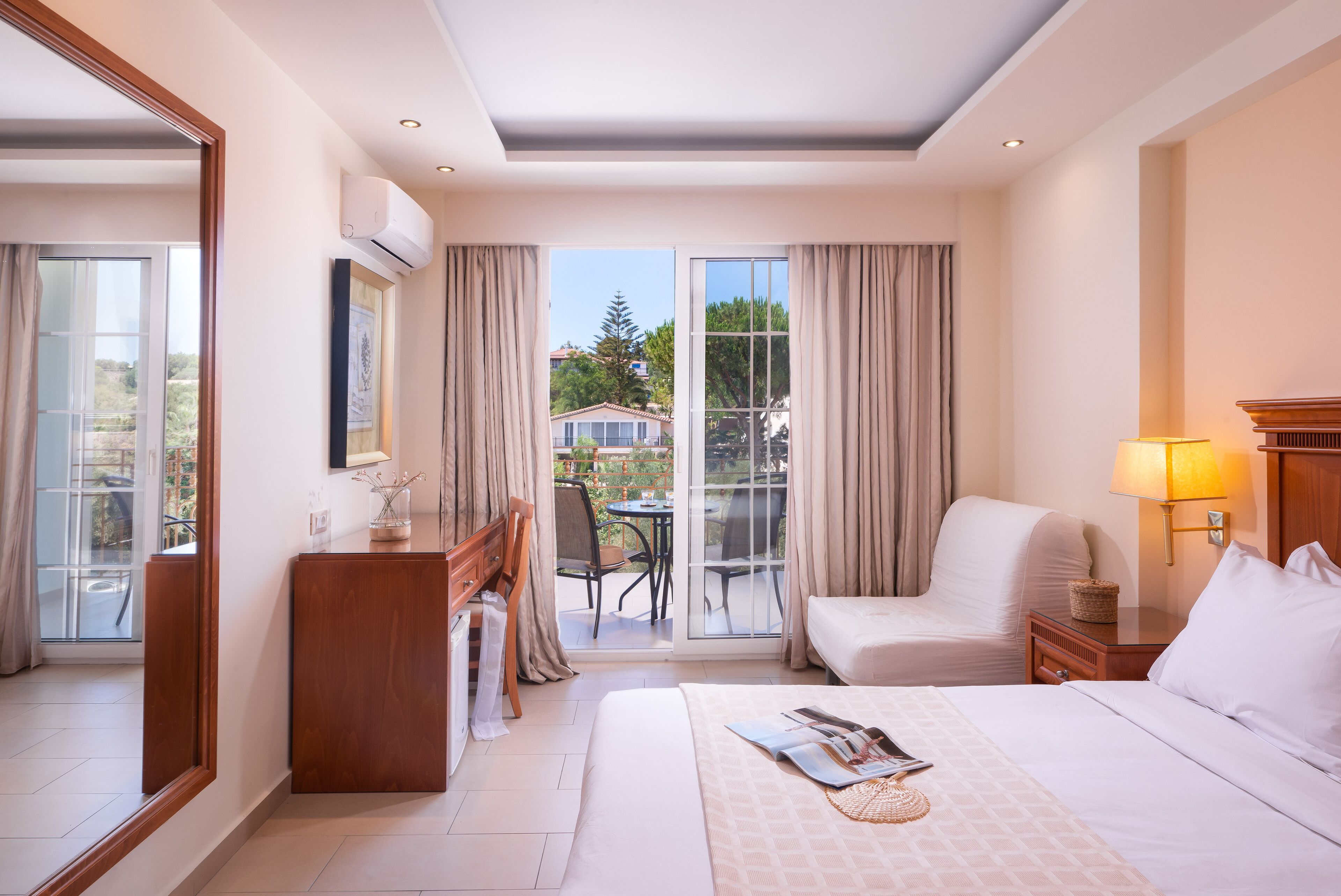 Habitación de hotel con cama, escritorio, silla, mesa y balcón con vistas al exterior.