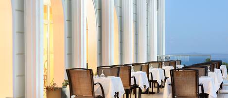 A restaurant with tables and chairs arranged outdoors, overlooking a scenic view.