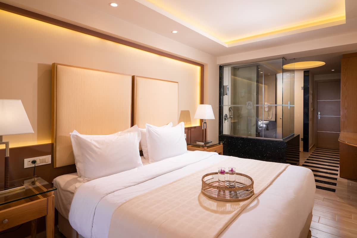 Une chambre d’hôtel avec un grand lit, des lampes de chevet, une douche en verre et un plateau avec des verres et une bouteille.