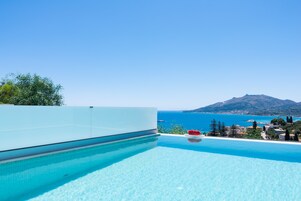 Cielo azzurro, piscina e vista sul mare e su una montagna.
