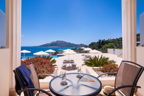 A balcony with a view of the sea, lounge chairs, umbrellas, and a table with glasses. - Avalon Palace Hotel by GHH (Zakynthos)