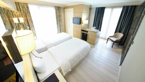 Une chambre d’hôtel avec deux lits, un bureau avec une télévision, une chaise et une fenêtre avec des rideaux.