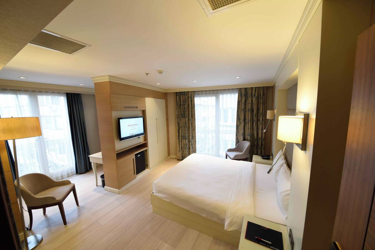A hotel room with a large bed, a TV, a desk, and a chair.