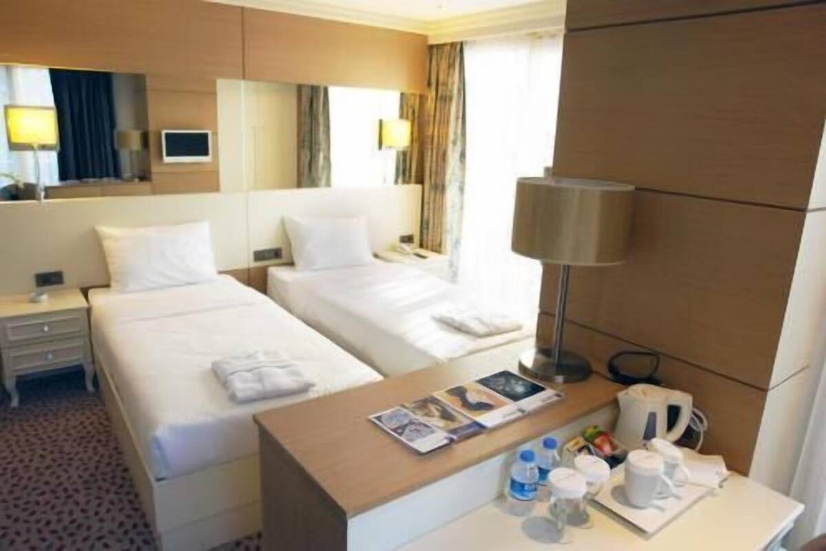 A hotel room with two beds, a desk with a lamp, a coffee maker, and a magazine.